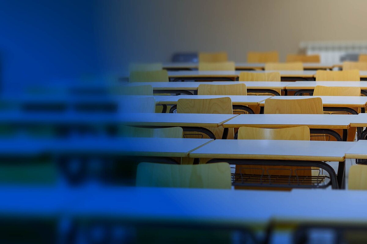 Tukša lekciju auditorija ar galdu rindām un krāsainiem krēsliem.