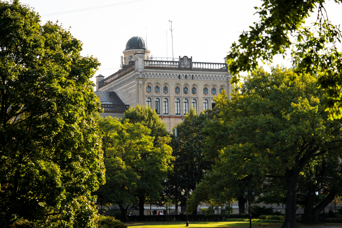 Latvijas Universitātes galvenā ēka Raiņa bulvārī 19, skatoties caur parka kokiem.