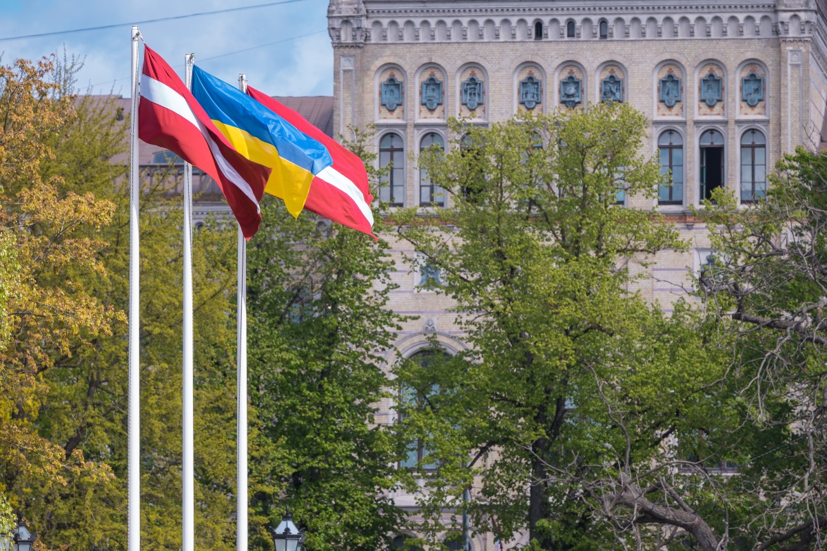 Karogi un aiz kokiem daļēji redzama Latvijas Universitātes ēka Raiņa bulvārī 19
